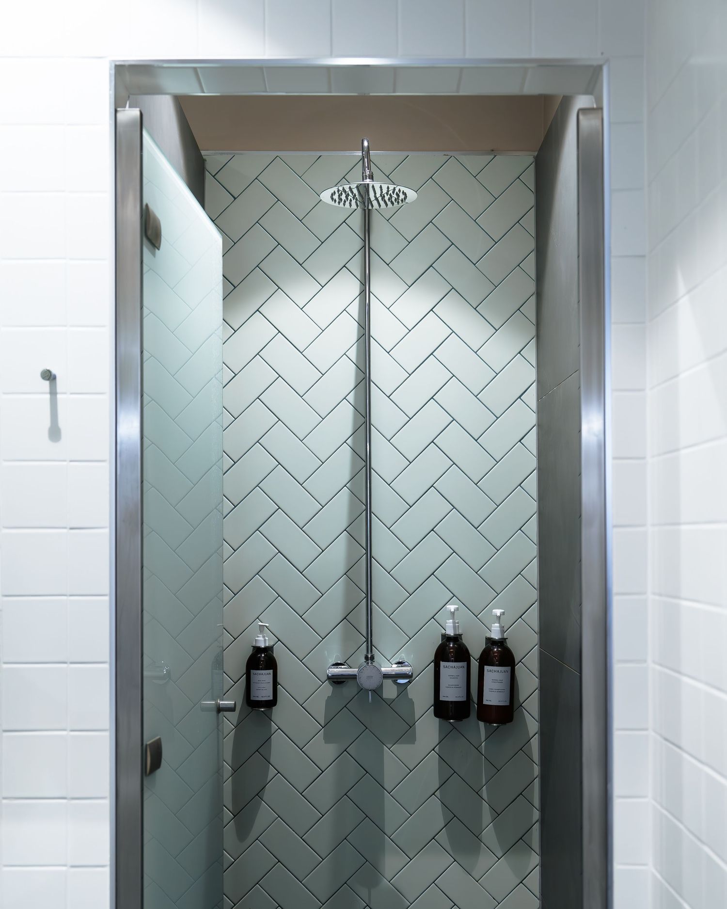 Modern shower with herringbone green tile, rain showerhead, and glass door in a clean bathroom.