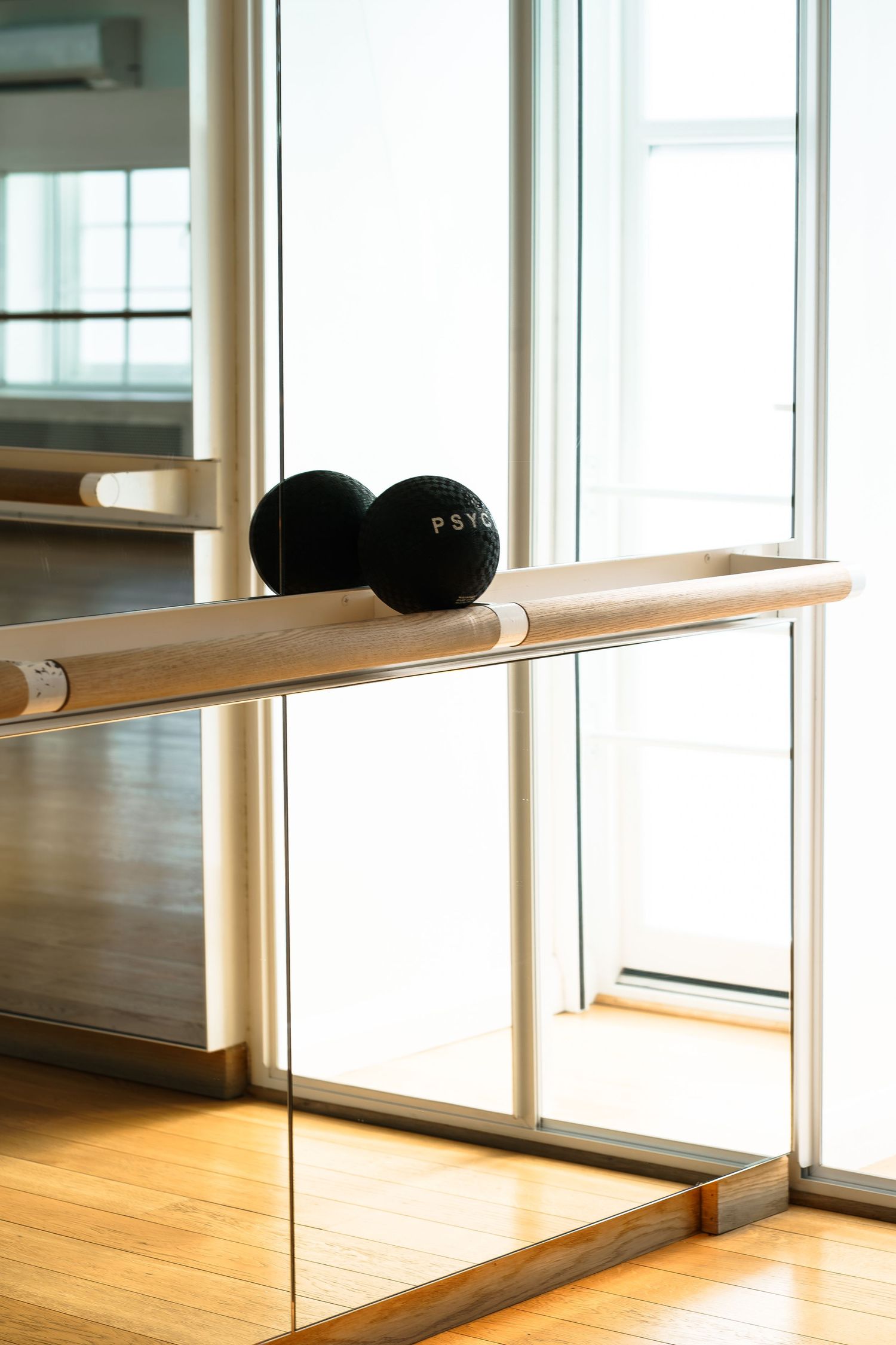 Psycle branded black exercise balls resting on a wooden ballet barre in a bright studio.