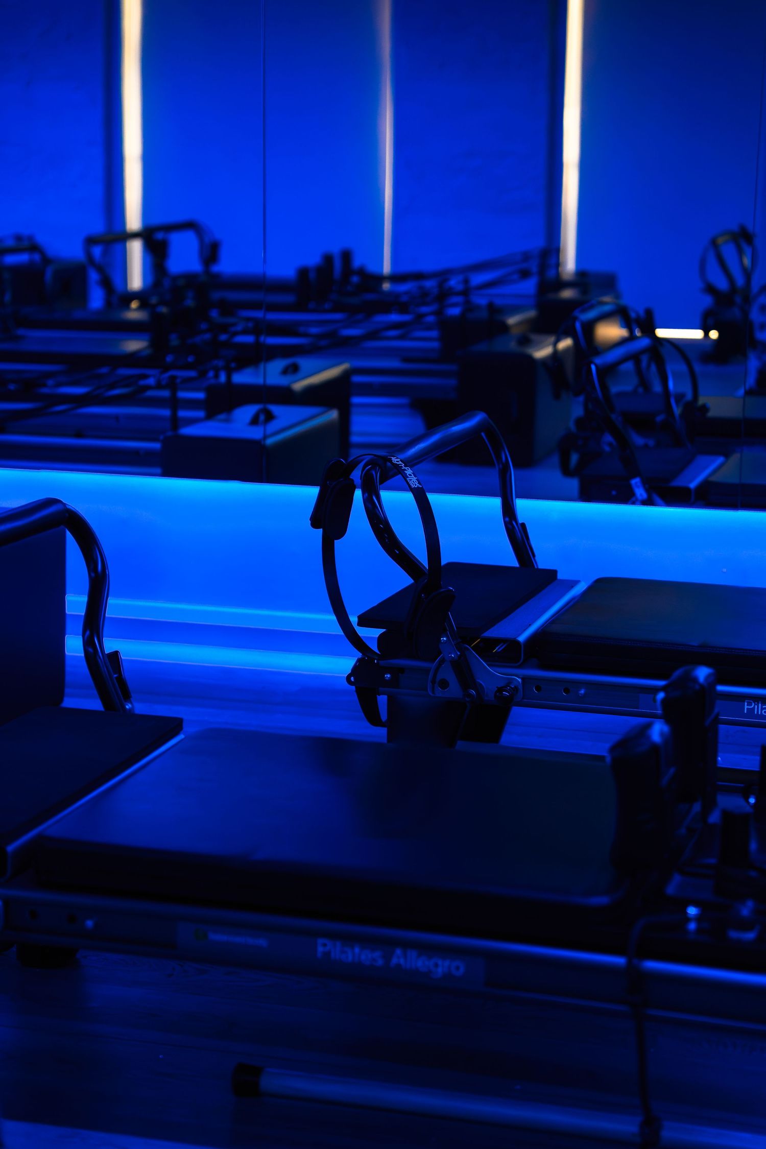 Pilates reformer machines lined up in a modern studio with dramatic blue LED lighting creating an atmospheric workout space.
