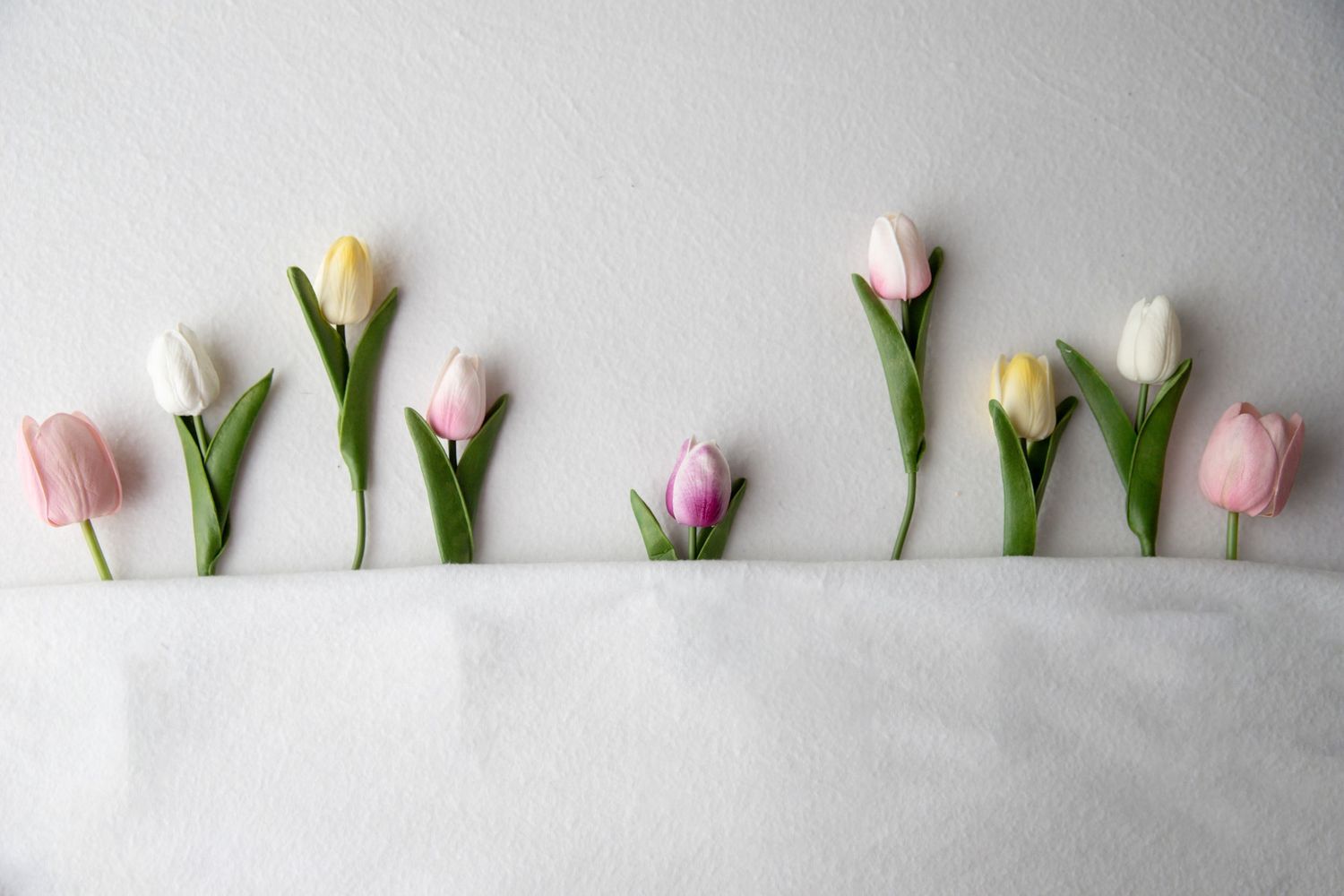 Colorful tulips in pink, yellow, and white arranged in a row on a white fabric background.