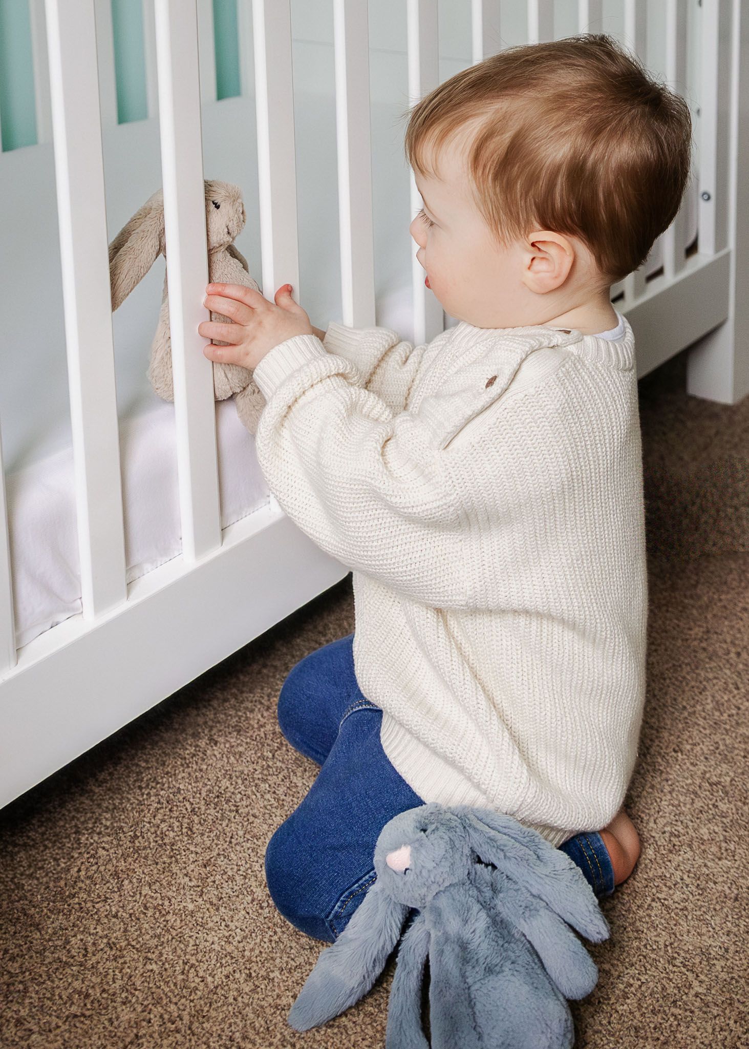 A toddler finds his favourite Jellycat rabbit toy in his cot during a relaxed photoshoot at home with a in home Bristol family photographer.