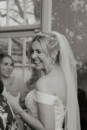 Black and white portrait of a laughing bride wearing a floral hair accessory and veil at her wedding.