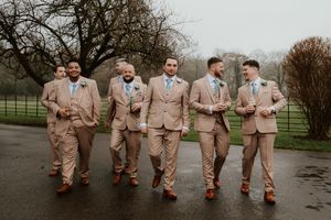 Groomsmen in matching tan suits with teal ties walking together on a rainy wedding day.