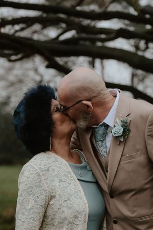 Couple sharing a romantic kiss outdoors, groom in tan suit with succulent boutonniere.