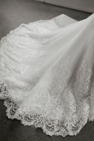 Close-up of intricate floral lace embroidery on a white wedding dress train spread on floor.