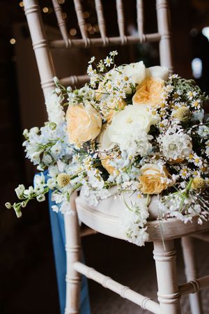 Romantic bridal bouquet of peach roses, white flowers, and daisies resting on a wooden chiavari chair.