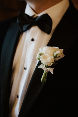 Groom in black tuxedo with bow tie wearing an elegant white rose boutonniere on his lapel.