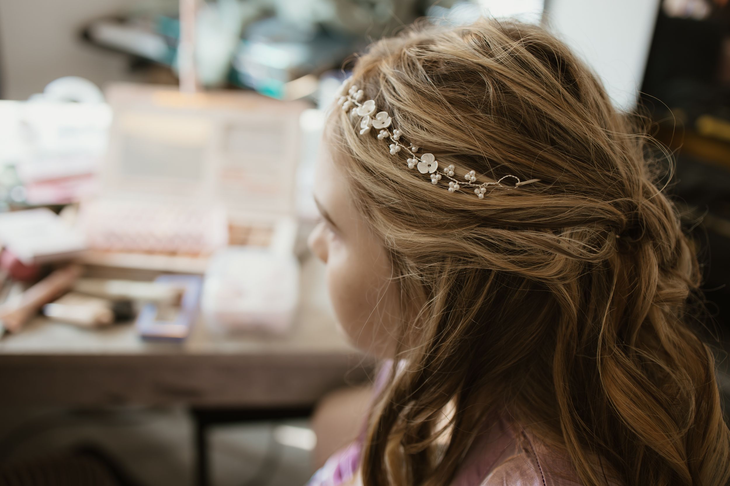 Close-up of young girl with elegant floral hair accessory at vanity mirror.