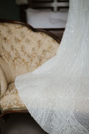 Sparkling beaded white wedding dress draped over a vintage sofa.