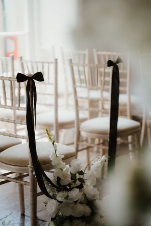 Wedding ceremony aisle with chiavari chairs decorated with black ribbon bows and white floral arrangements.
