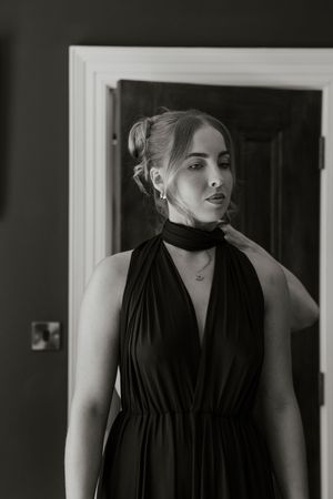 Black and white portrait of a woman in a black halter dress by a door.
