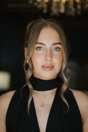 Young woman with blue eyes in black halter dress with gold necklace.