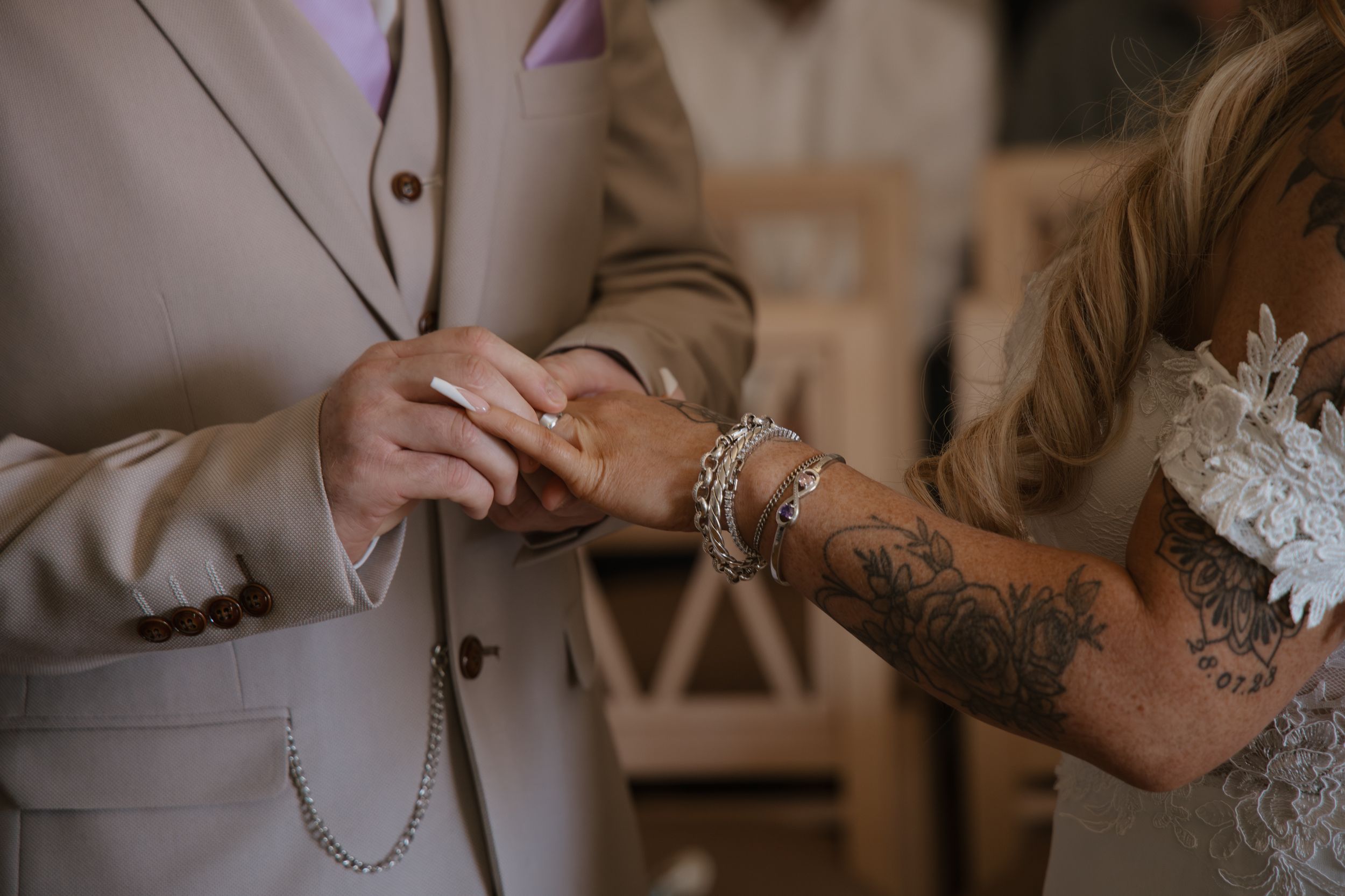 Close-up of groom placing wedding ring on tattooed bride's hand during wedding ceremony.