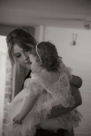 Bridesmaid tenderly holding a young flower girl in a white tulle butterfly dress at a wedding ceremony.