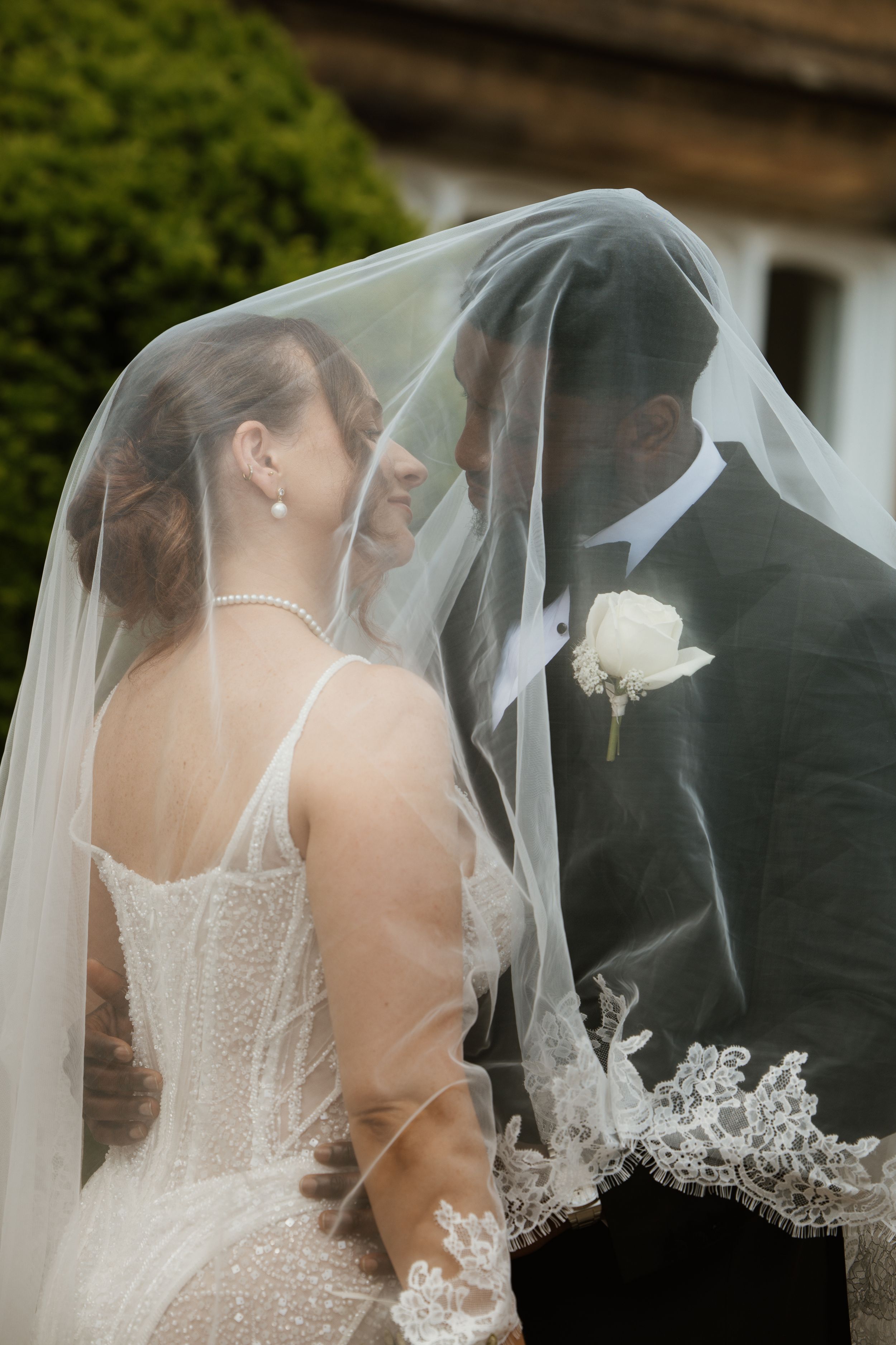 Bride and groom sharing an intimate moment under a lace wedding veil outdoors at their wedding.