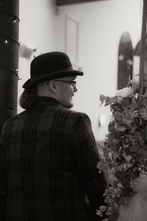 Elegant wedding guest in bowler hat and plaid jacket viewing floral arrangements at a wedding venue.