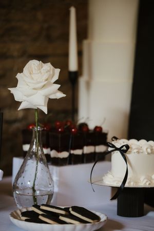 Elegant wedding dessert table featuring a white rose, black candles, Oreo cookies, and white cake.