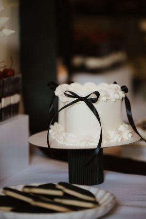 Elegant white wedding cake with black ribbon bow on a black cake stand with black and white cookies.