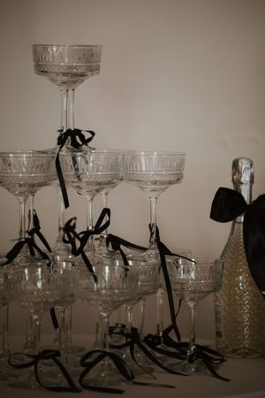 Crystal champagne tower glasses with black ribbon bows next to a decorated bottle.