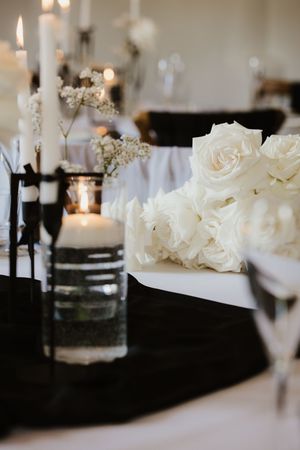 Elegant black and white wedding reception table with white roses, candles, and black runner.