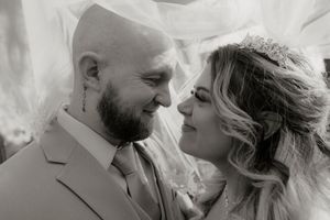 Black and white romantic close-up of bride and groom nearly kissing under a flowing wedding veil.