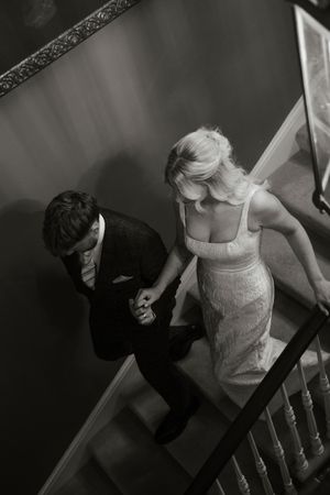Black and white aerial view of bride and groom holding hands descending elegant staircase.