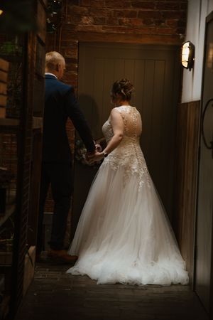 Bride and groom holding hands walking through a rustic doorway at their wedding venue.