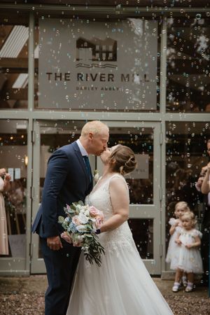 Bride and groom sharing a romantic kiss outside The River Mill Darley Abbey amid floating bubbles.