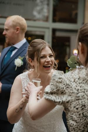 Joyful bride in lace wedding dress laughing and holding champagne glass during wedding reception.