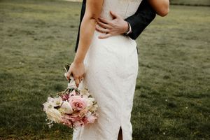 Close-up of bride and groom embracing outdoors, bride holding pink and white rose bouquet.