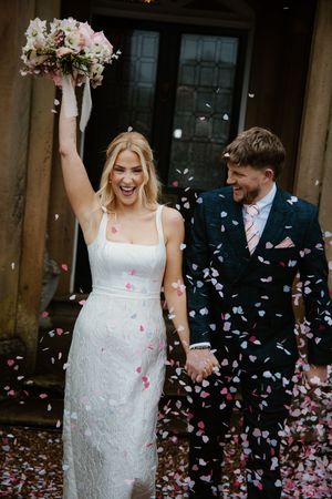Joyful newlyweds celebrating with pink confetti outside wedding venue.