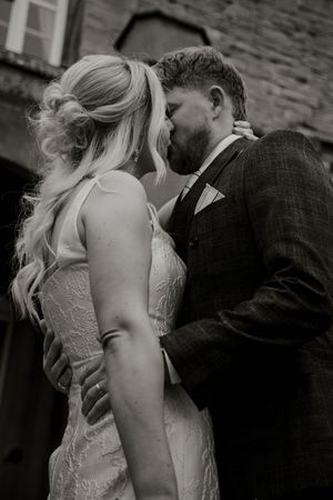 Black and white romantic kiss between bride and groom outside stone venue.