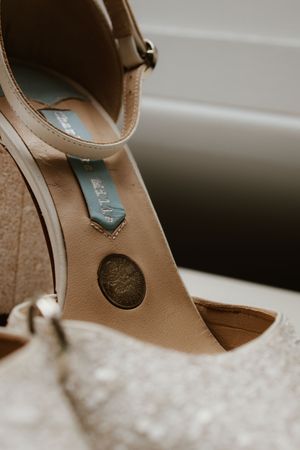Close-up detail of nude bridal heels with coin charm and teal ribbon lucky token.