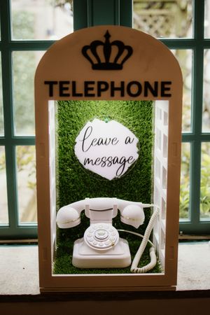 Decorative wedding telephone booth with white rotary phone and leave a message sign.