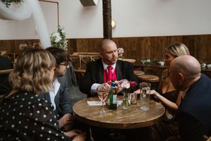 Wedding guest in red tie performing close-up magic tricks at a round table during reception.