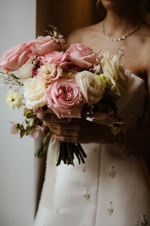 Bride holding a romantic wedding bouquet of pink and cream roses in a white gown.