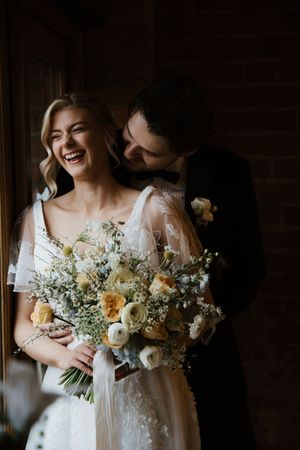 Joyful bride and groom sharing an intimate moment, bride holding a bouquet of peach, white, and blue flowers.