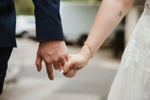 Close-up of bride and groom holding hands showing wedding rings and gold bracelet.