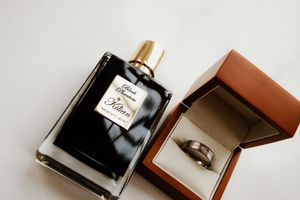 Kilian Black Phantom perfume bottle beside a silver wedding band in a brown ring box.