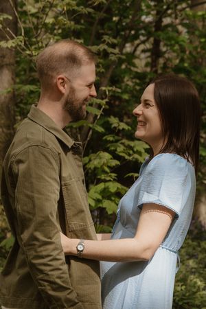 Happy couple smiling at each other while holding hands in lush green garden setting.