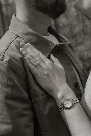 Black and white close-up of womans hand with engagement ring resting on mans chest.