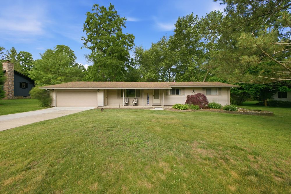 Ranch-style home with large front lawn, mature trees, attached garage, and welcoming covered entryway on a sunny day.