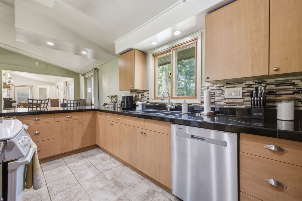 Spacious kitchen with light wood cabinetry, dark granite counters, tile backsplash, and stainless steel dishwasher.