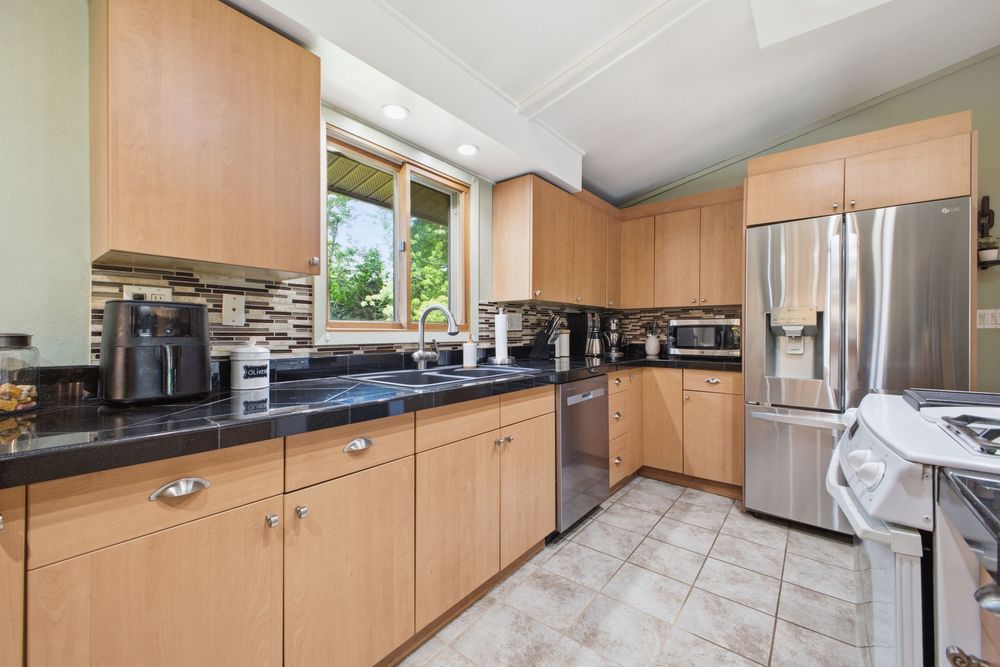 Modern kitchen with light wood cabinets, dark granite countertops, stainless steel appliances, and tile backsplash.