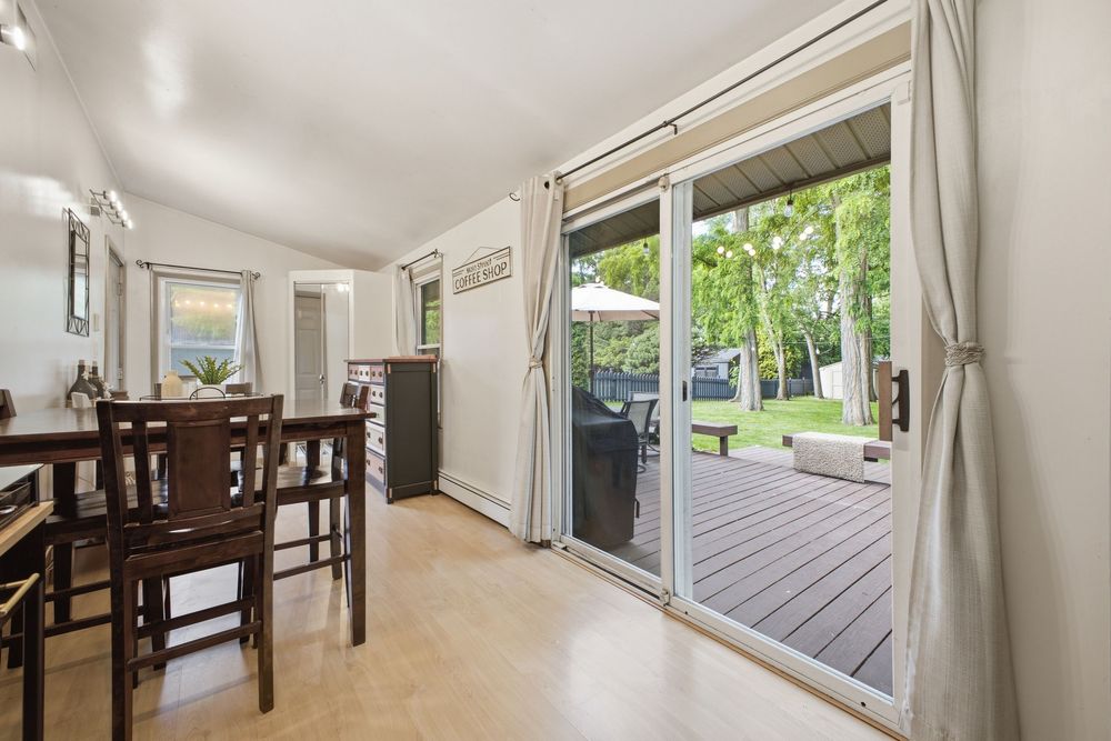 Bright dining area with sliding glass doors opening to a wood deck surrounded by lush green trees.