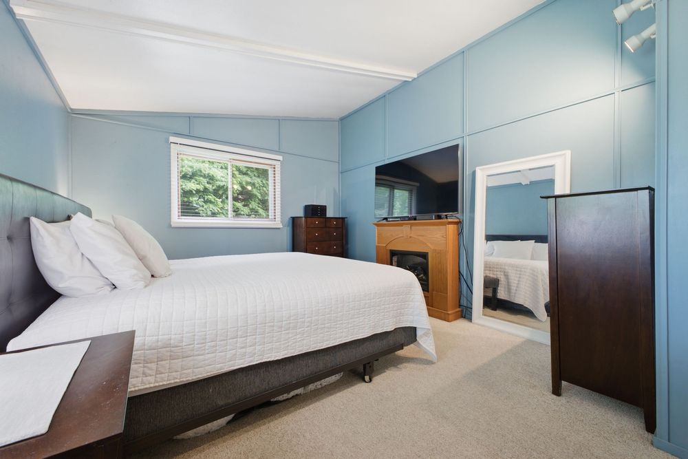 Spacious bedroom with blue walls, large white bed, carpeted floors, and a decorative fireplace with mirror.