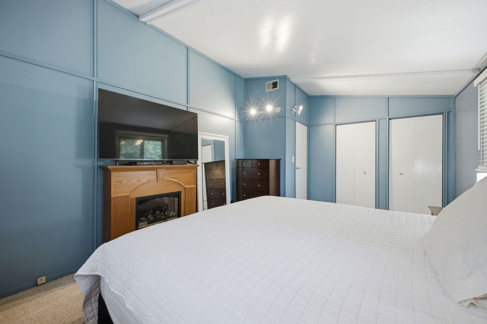 Blue-walled bedroom with white bedding, built-in cabinets, and a decorative fireplace with wood mantel.
