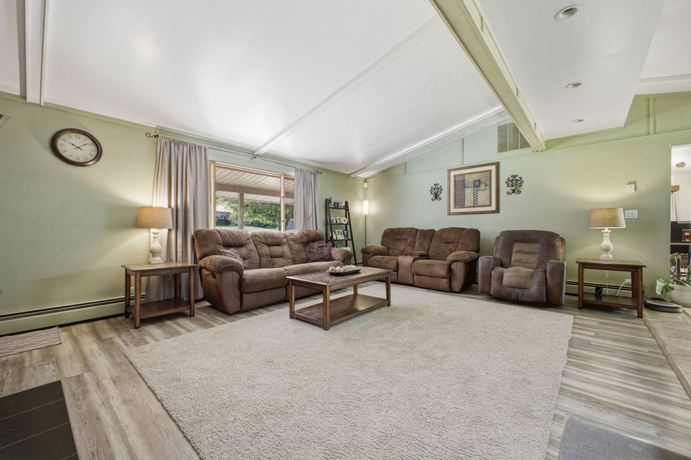 Spacious living room with vaulted ceilings, green walls, brown recliner sofas, area rug, and hardwood floors.