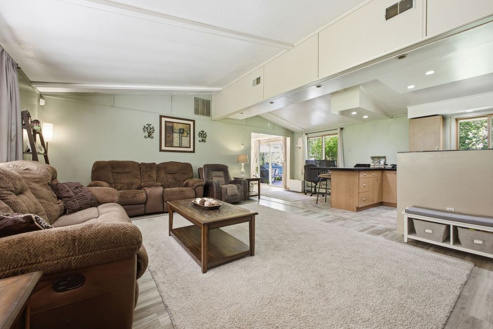 Spacious living room with brown recliner sofas, beige carpet, wood coffee table, and open layout leading to kitchen area.