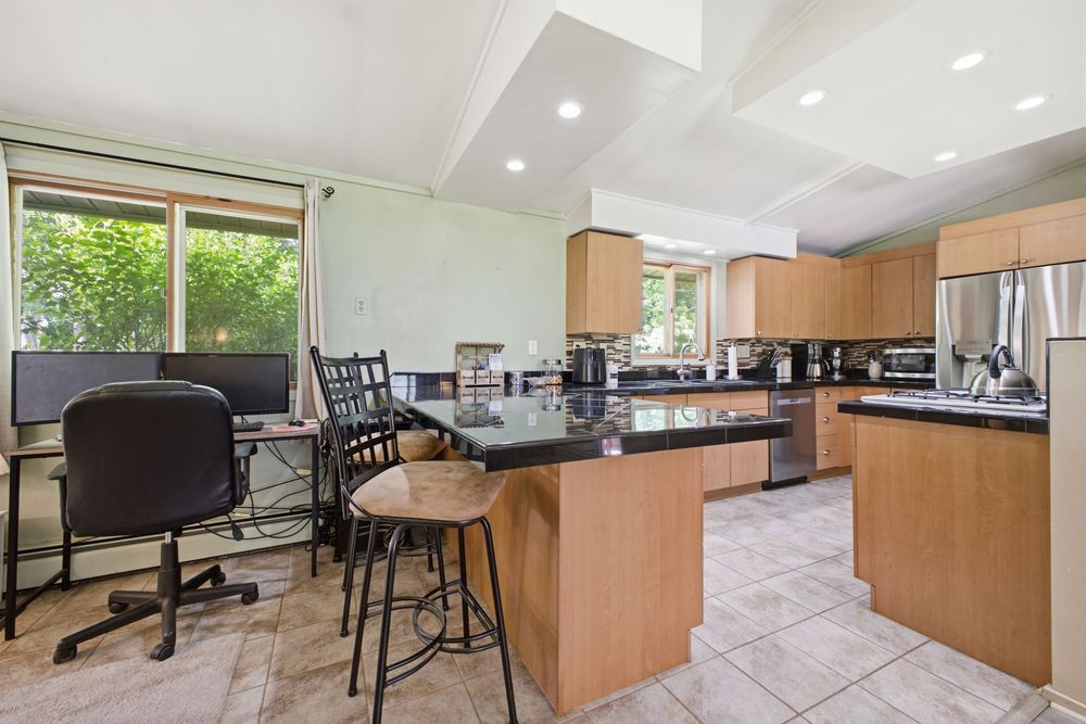 Bright kitchen with light wood cabinets, granite island with bar seating, stainless appliances, and adjacent dining area with garden view.
